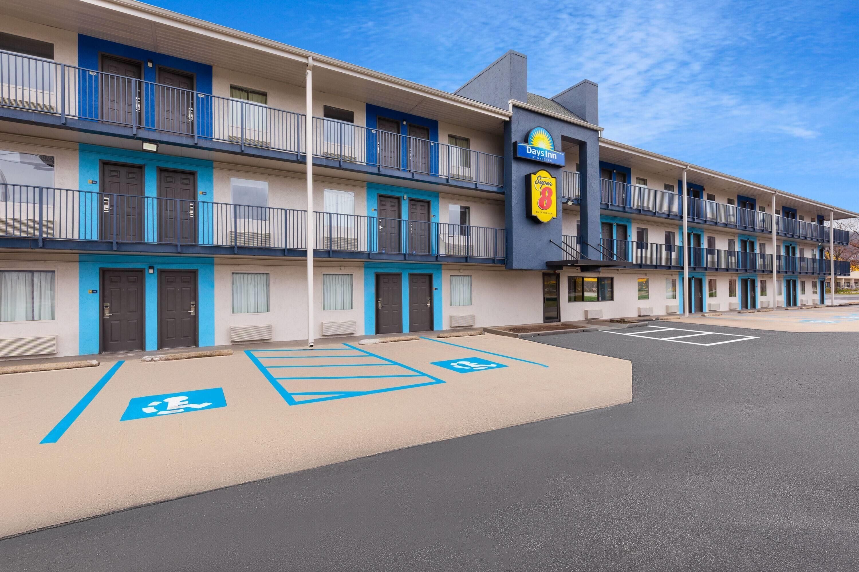 Un motel de varios pisos con un letrero de Days Inn, estacionamiento accesible para sillas de ruedas y una paleta de colores azul y blanco.