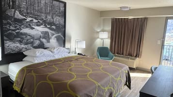 Une chambre d’hôtel avec un grand lit, un bureau, une chaise, une lampe et un grand tableau encadré représentant un paysage forestier.