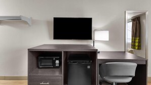 A hotel room with a desk, a flat-screen TV, a microwave, a mini-fridge, a chair, and a window with curtains.