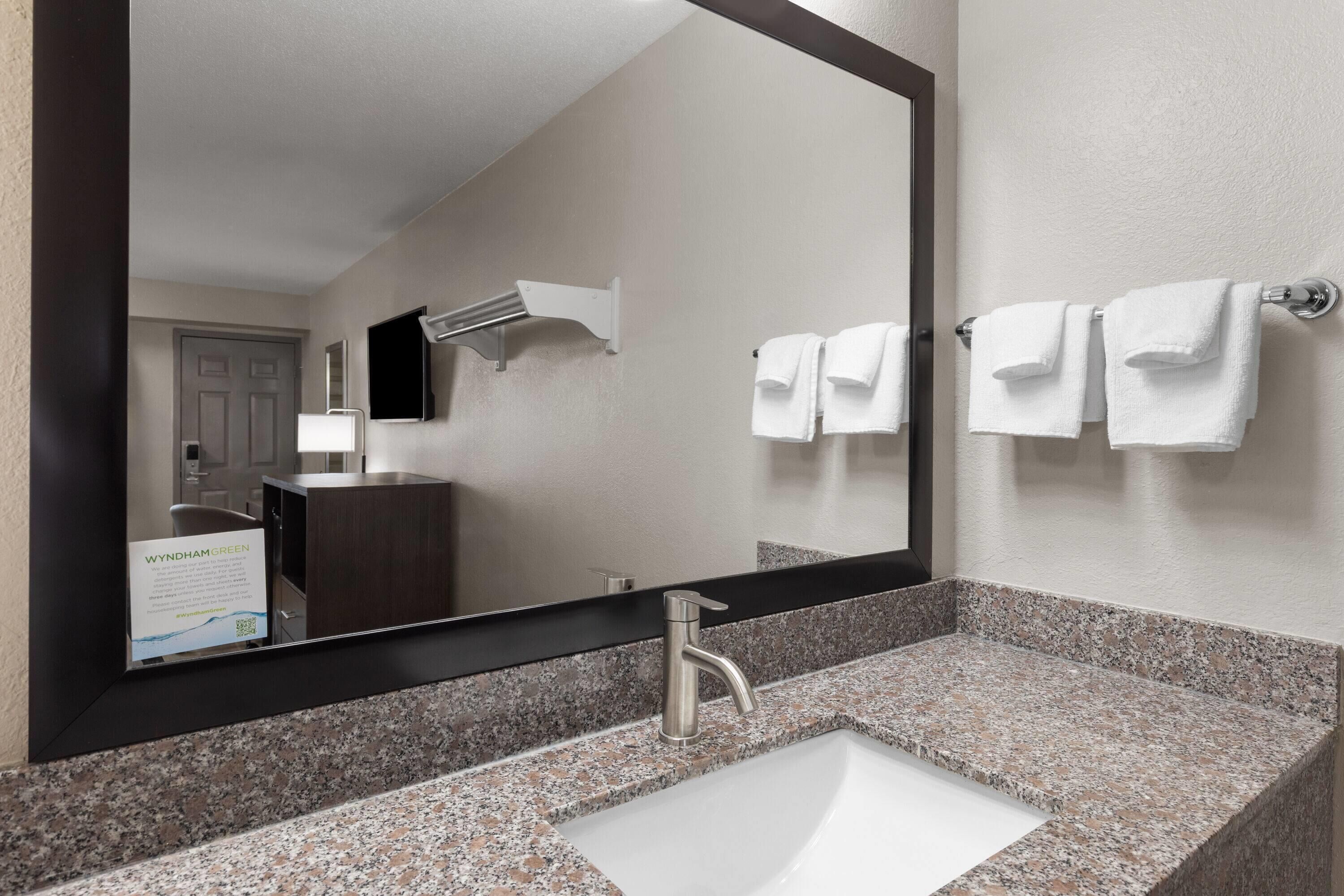 A bathroom with a large mirror, a sink, and two towels hanging on a towel rack.