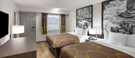 A hotel room with two beds, a desk, a TV, and large windows with curtains.