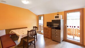 A compact kitchen with a dining area, wooden cabinets, a microwave, and a sliding glass door to the outside. - “Appartamento Legnameir Bait da Rez” with Balconies & Wi-Fi (Livigno)