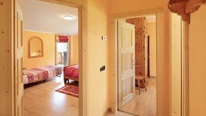 A room with wooden floors, a bed with a red blanket, a mirror on the wall, and a door leading to another room. - “Appartamento Legnameir Bait da Rez” with Balconies & Wi-Fi (Livigno)