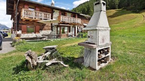 A rustic wooden building with a balcony, outdoor seating, and a stone chimney. - “Appartamento Legnameir Bait da Rez” with Balconies & Wi-Fi (Livigno)