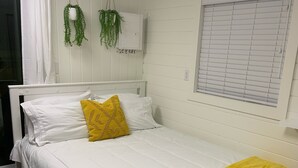 Een slaapkamer met een bed, witte beddengoed, een gele plaid en twee hangplanten.