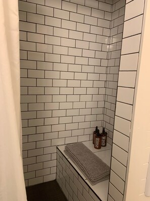 Une salle de bain avec des carreaux de céramique blancs rectangulaires, un porte-serviettes et deux bouteilles étiquetées « Rinçage » sur une étagère.