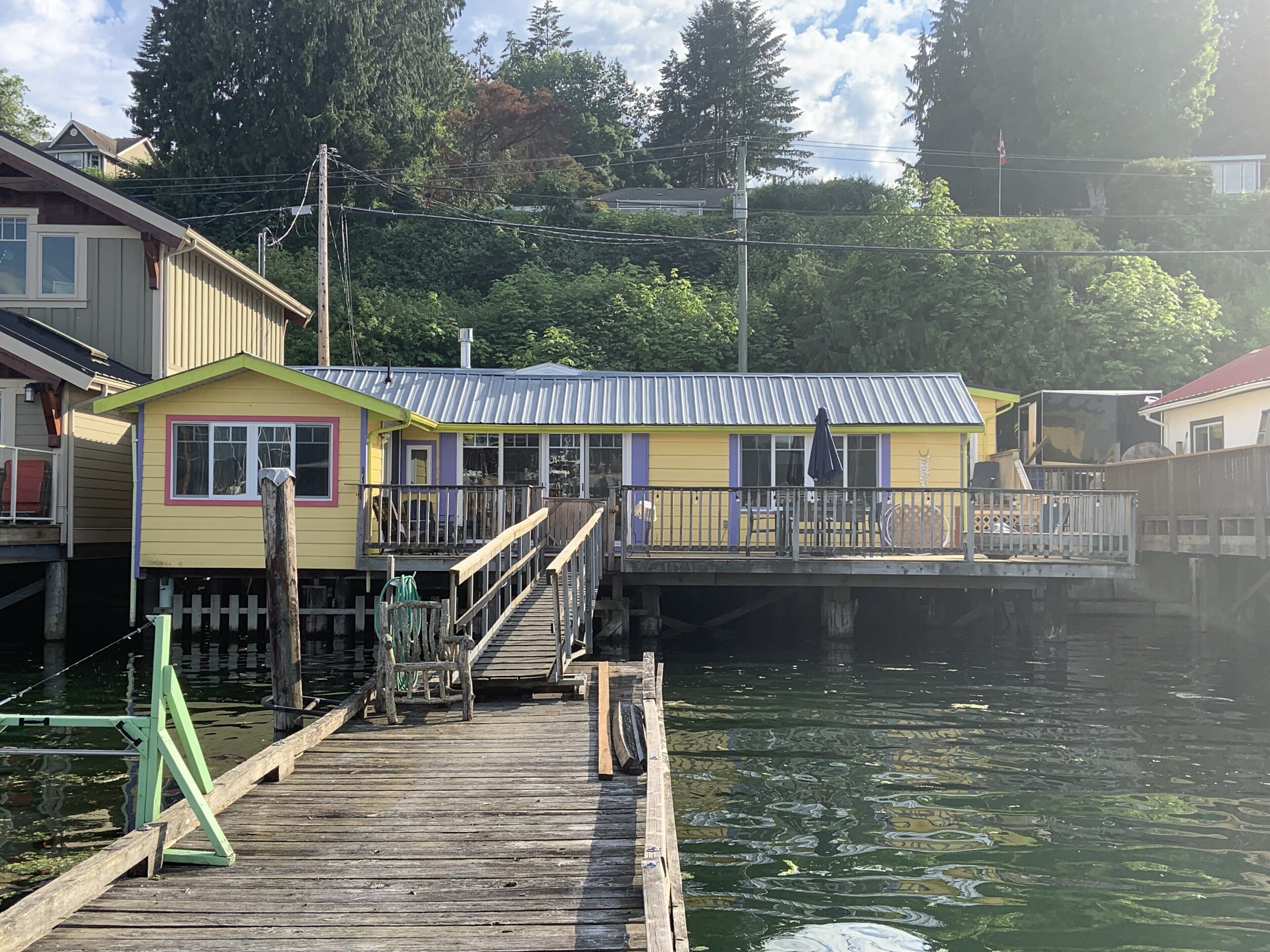 A dock leading to a yellow building with a metal roof, surrounded by water and trees.