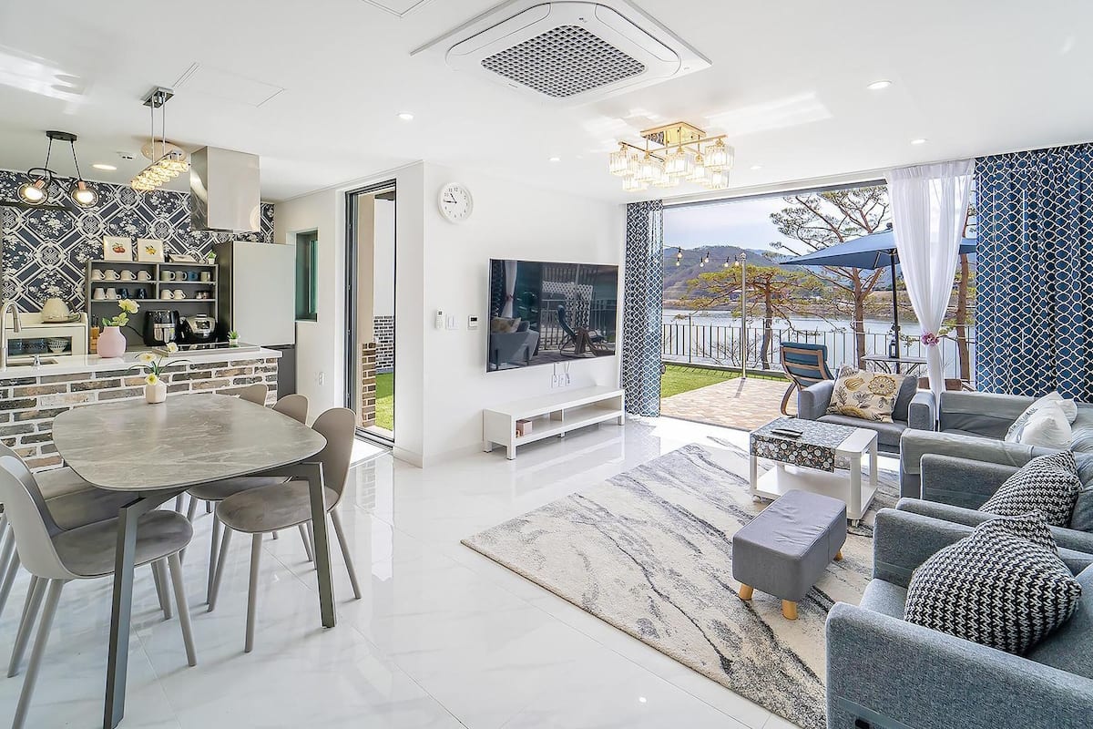 A modern living space with a dining area, kitchen, and a large window overlooking a scenic outdoor area.