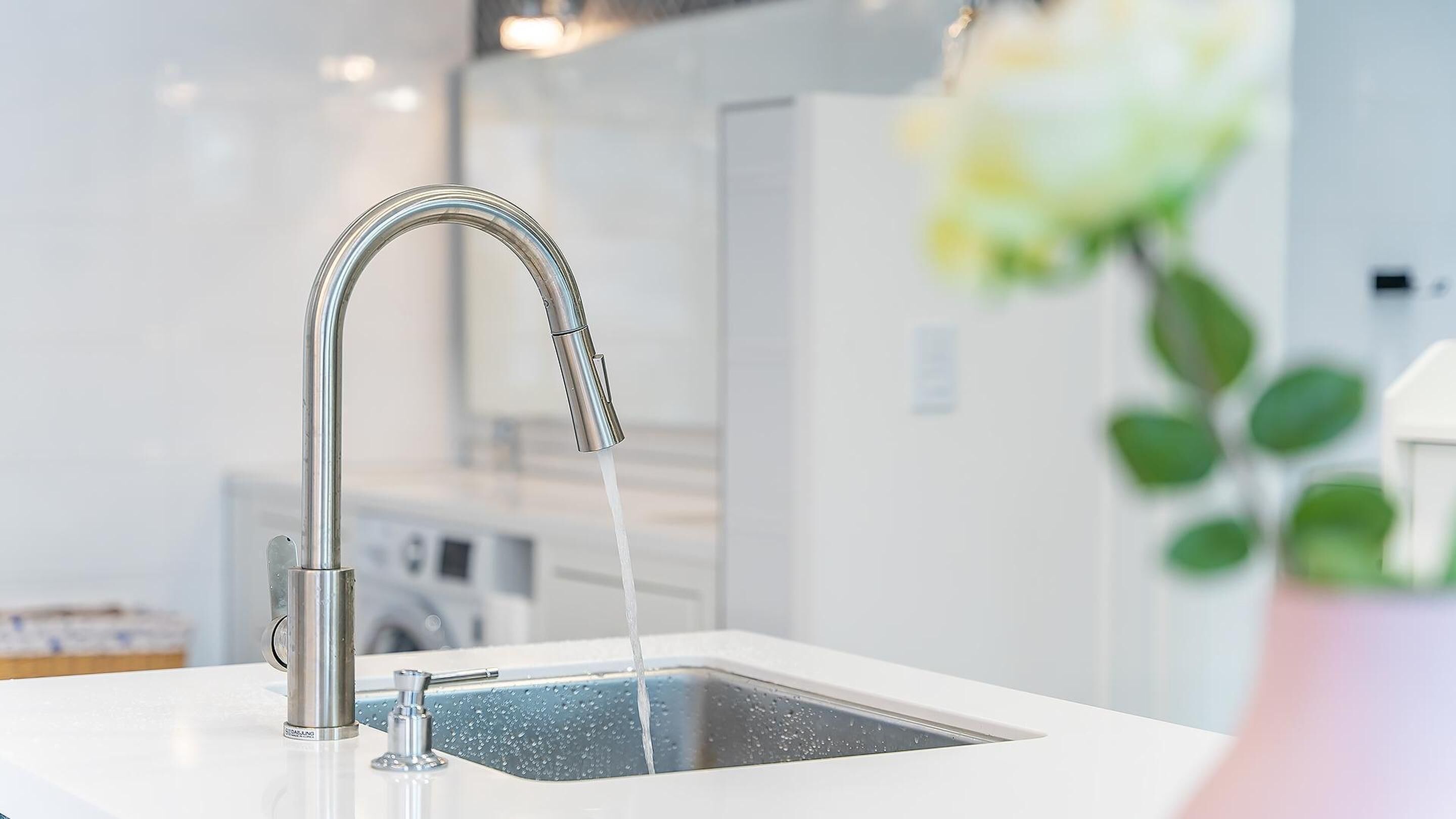 Une cuisine moderne dotée d’un robinet en acier inoxydable et d’un plan de travail blanc.