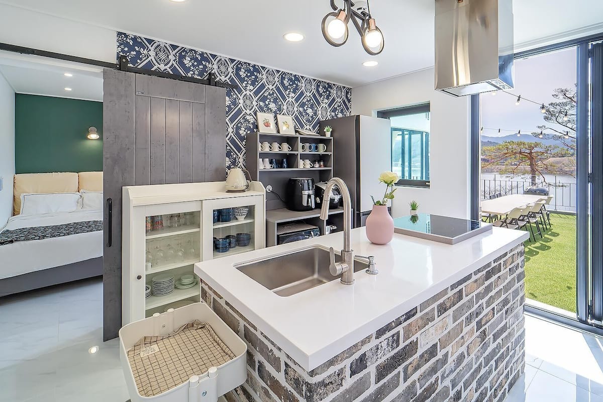 A modern kitchen with a large island, built-in shelves, and a view of the outdoors.