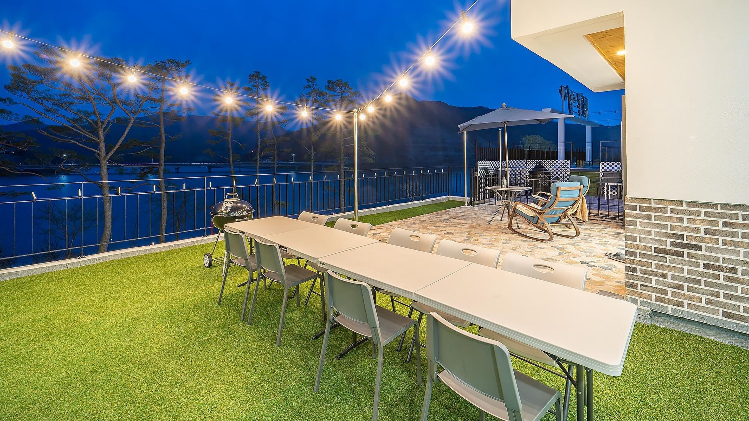 An outdoor patio with a long table and chairs, a grill, and string lights.
