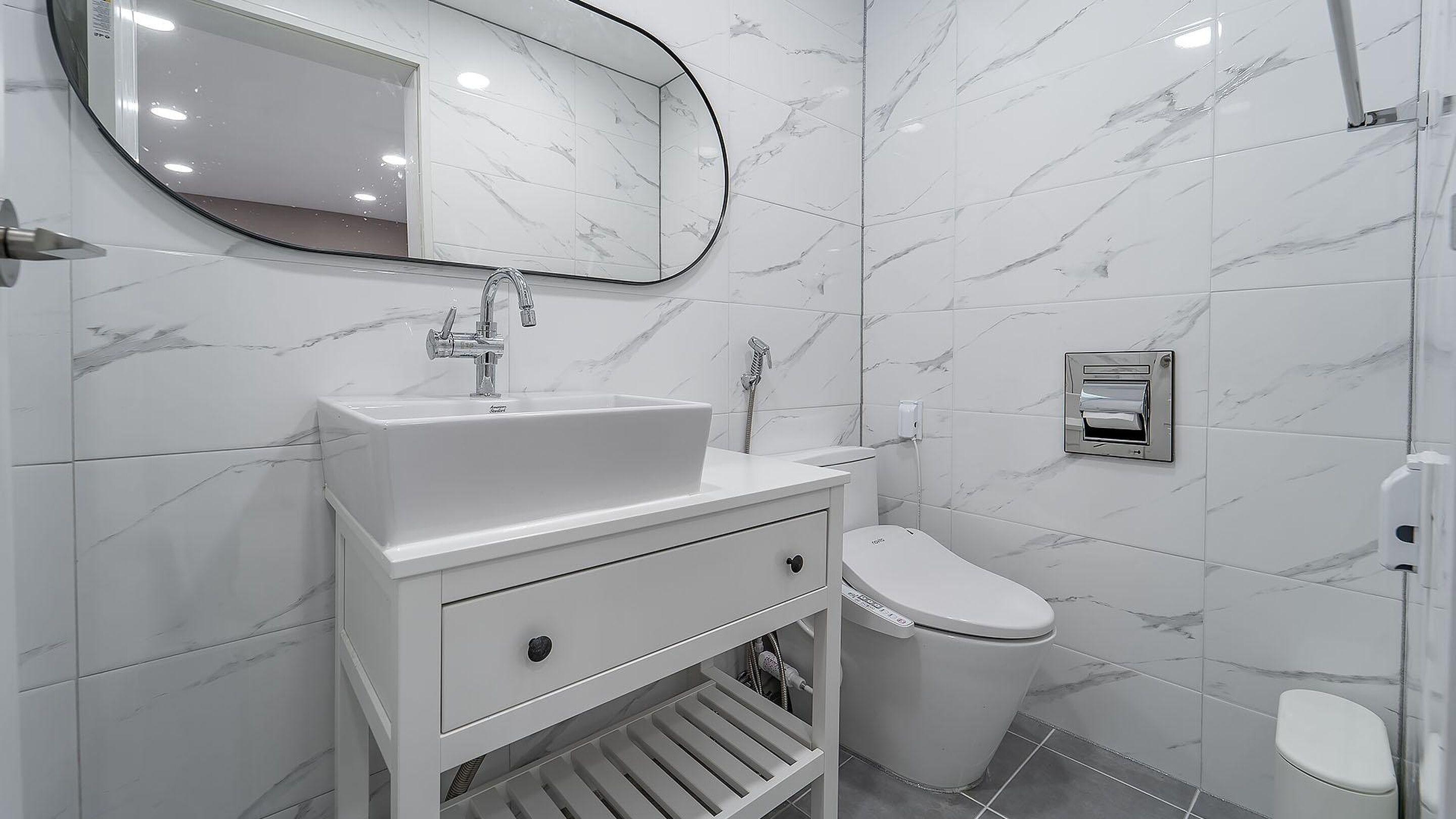 A modern bathroom with a white sink, mirror, and toilet.