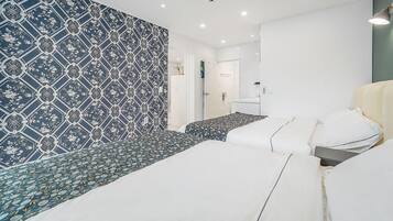 A modern hotel room with a patterned wallpaper, a bed with white linens, a small seating area, and a bathroom with a glass shower.