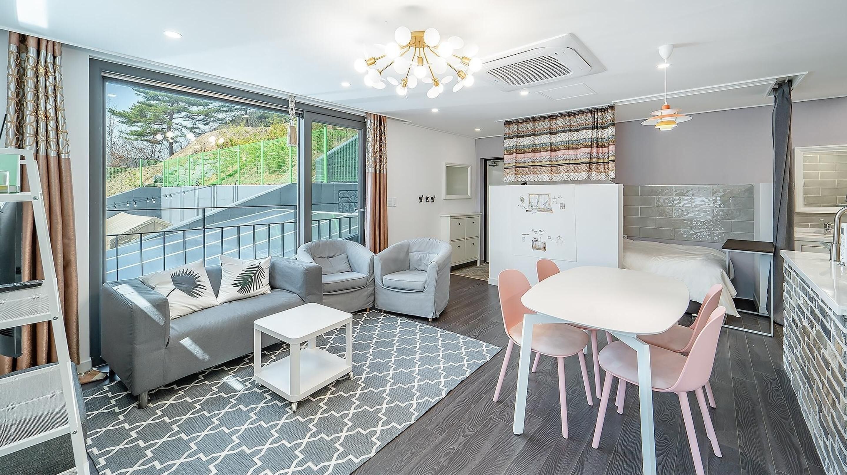 Una sala de estar moderna con un sofá gris, dos sillones, una mesita de centro y un comedor con una mesa blanca y sillas rosas.