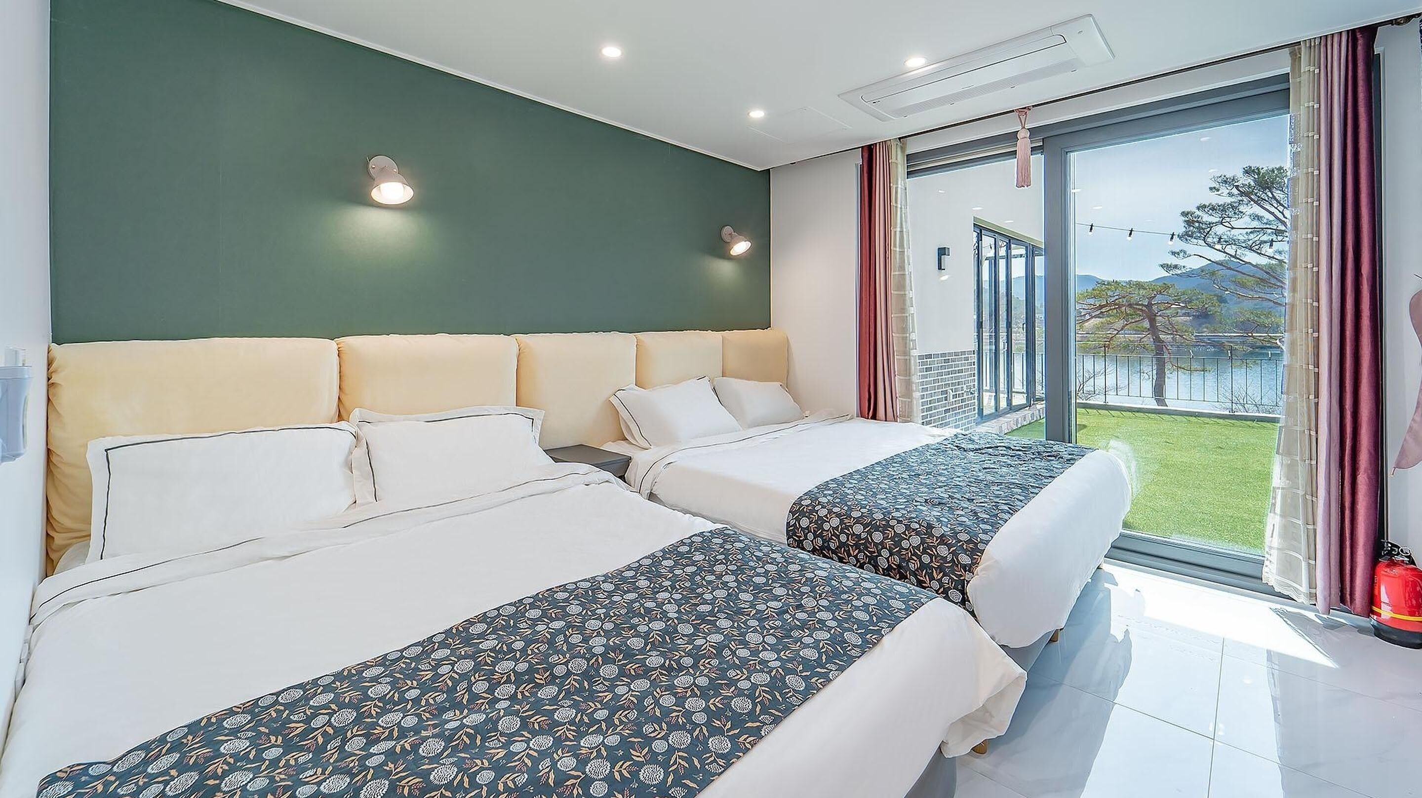Ett hotellrum med två sängar, en grön accentvägg och ett stort fönster med utsikt över omgivningarna.