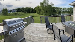 Terraza con una parrilla, sillas y una mesa, con vistas a un lago y follaje.