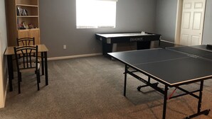 Una habitación con mesa de ping pong, estantería, escritorio y ventana.