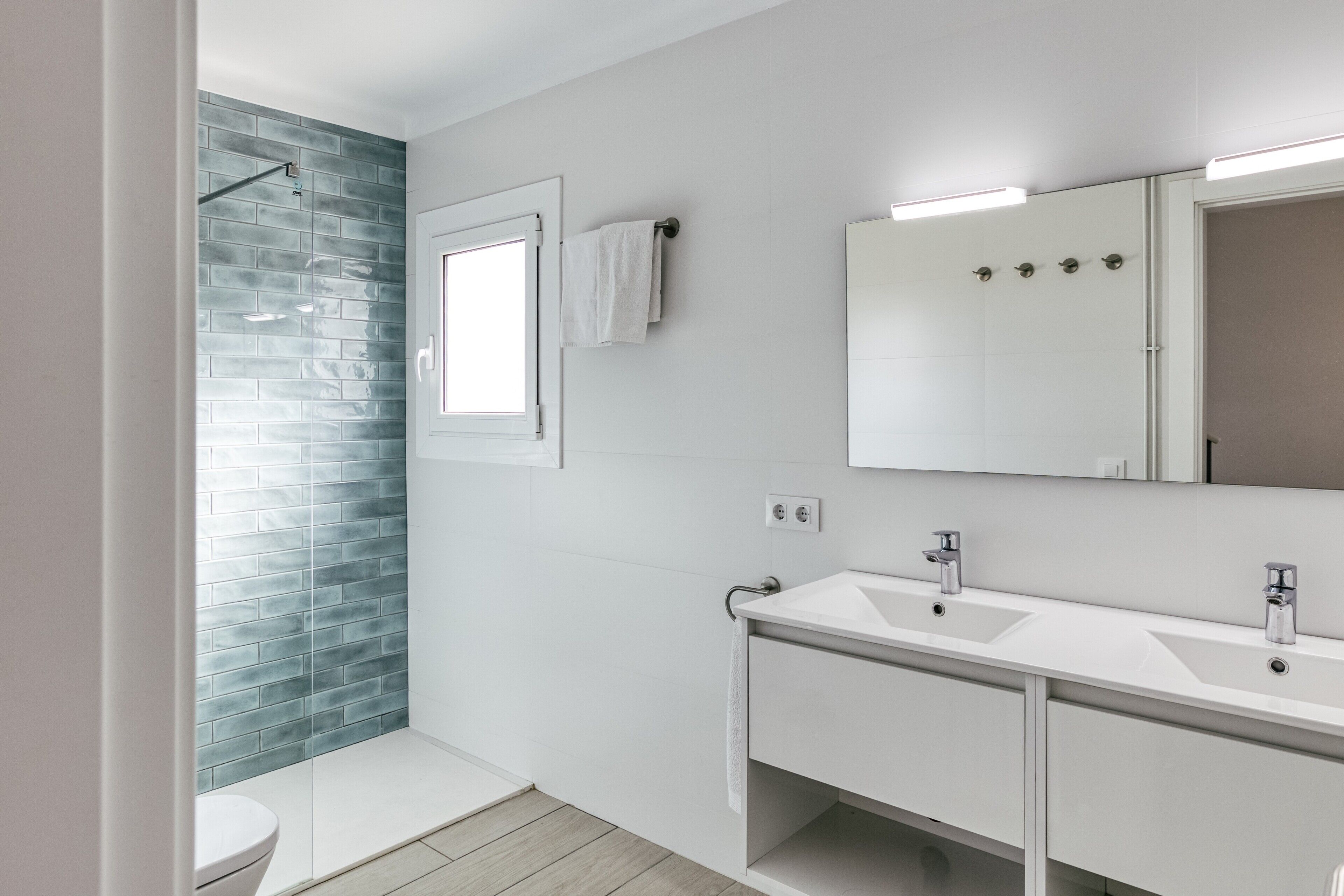 Een moderne badkamer met douche, twee wastafels, toilet en een grote spiegel.