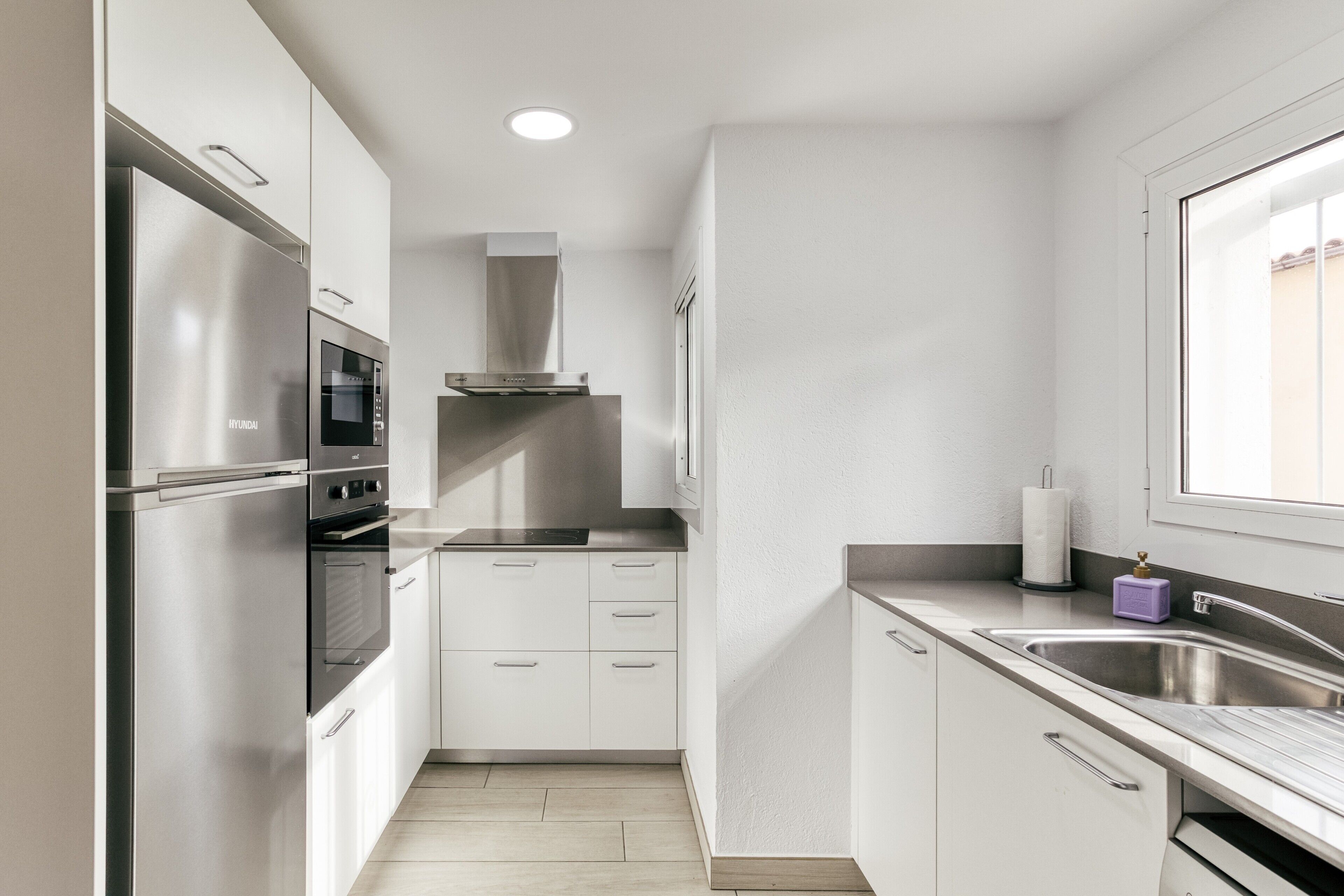 Una cocina compacta con gabinetes blancos, electrodomésticos de acero inoxidable y un ventanal que proporciona luz natural.
