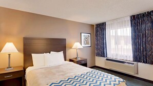 A hotel room with a large bed, two bedside tables with lamps, a window with curtains, and a wall-mounted air conditioner. - Travelodge Aberdeen WA (Aberdeen)