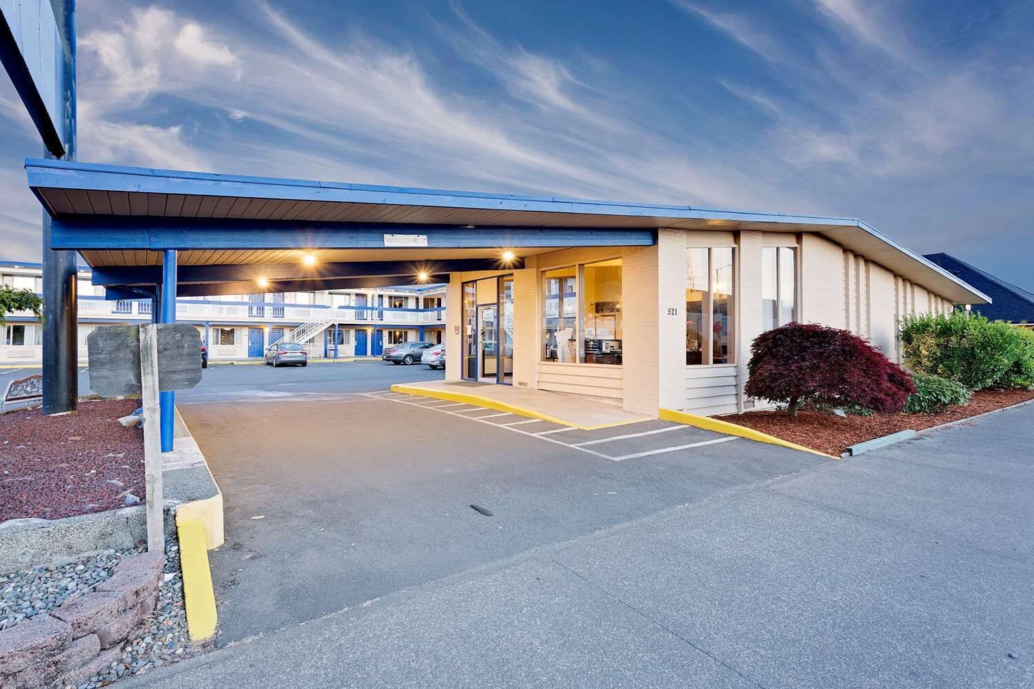 A motel with a covered parking area, a visible entrance, and a building with a flat roof.