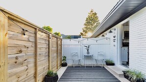 A wooden fence, a black and white striped rug, and a small table with chairs in a backyard.