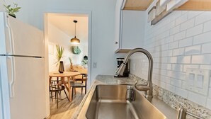 A modern kitchen with a stainless steel sink, white tiled backsplash, and wooden flooring.