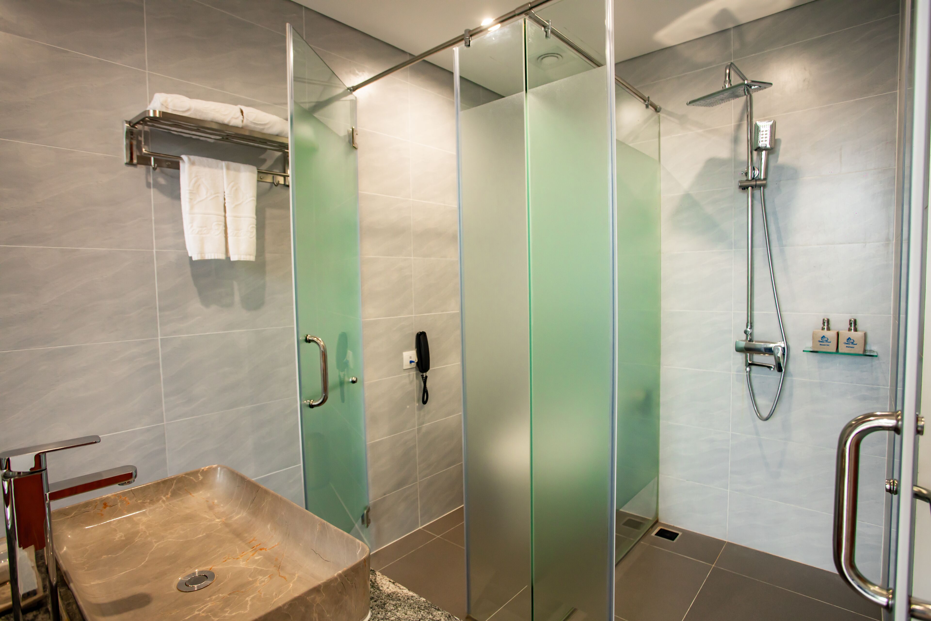Een moderne badkamer met een douchecabine van glas, een marmeren wastafel en een handdoekrek.