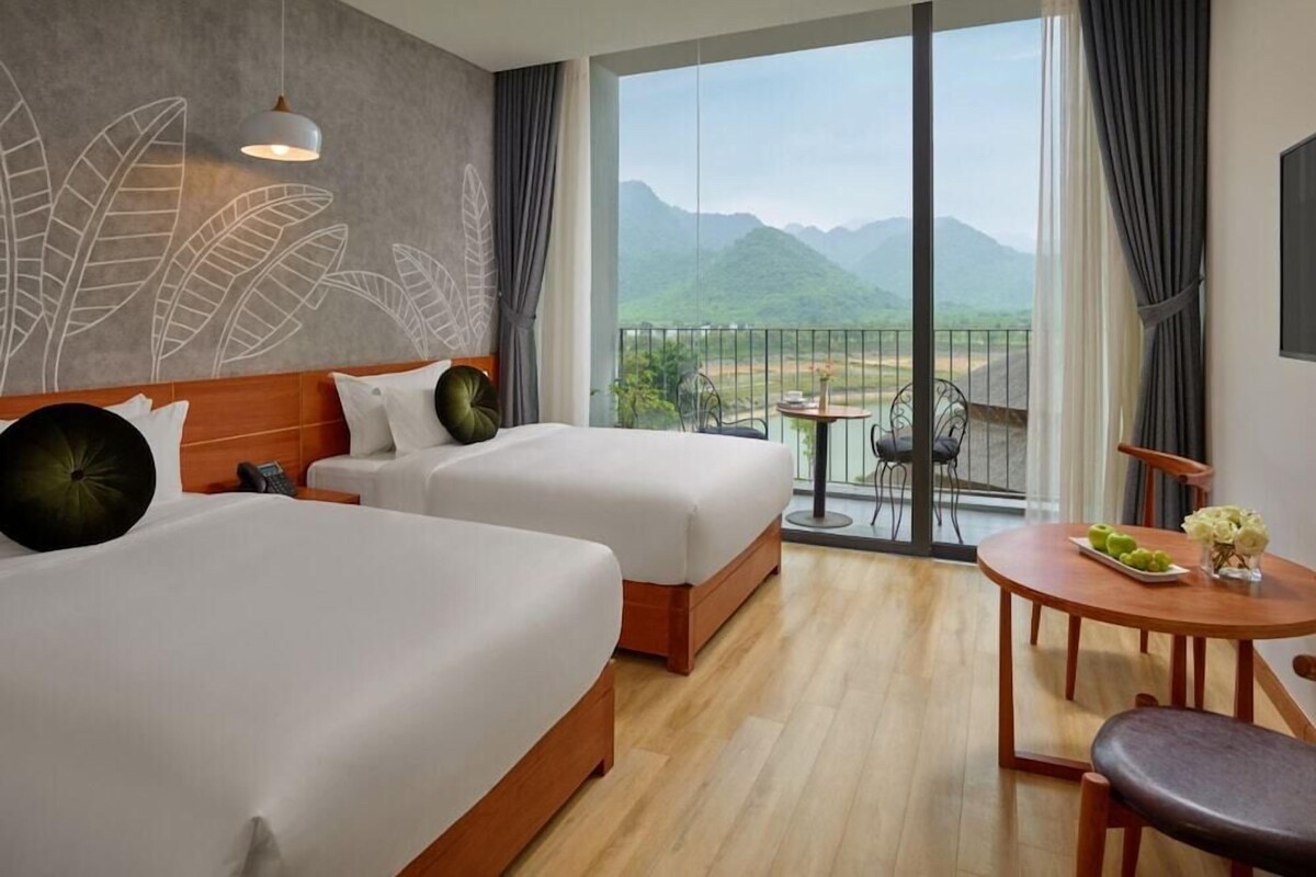 Ein Hotelzimmer mit zwei Betten, einem Balkon mit Tisch und Stühlen und Blick auf Berge.