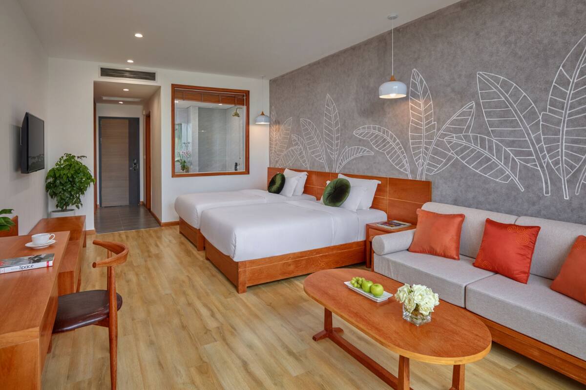 Quarto de hotel moderno com uma cama grande, um sofá, uma mesa de centro e um espaço de refeições.