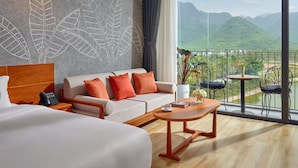 Une chambre d’hôtel avec un grand lit, un canapé, une table basse et une vue sur les montagnes depuis un balcon.