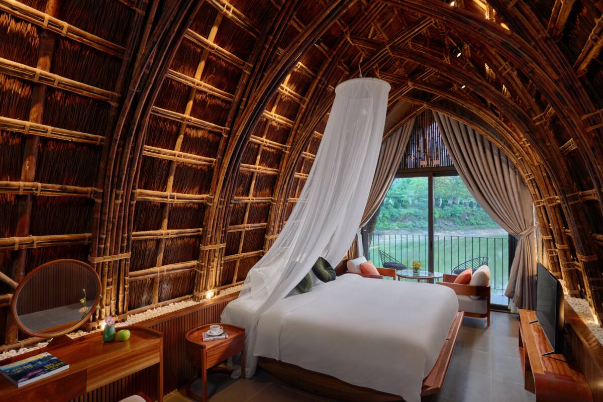 Quarto com cama, mesa de cabeceira, espelho e vista para o verde lá fora.