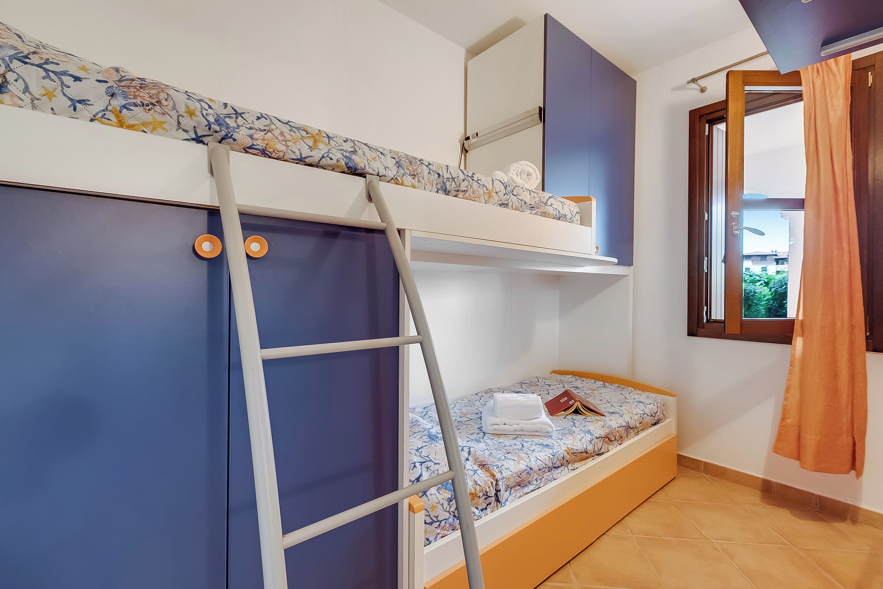 Habitación con literas, una escalera, una ventana con cortinas y un estante con objetos.