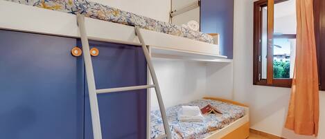 Habitación con literas, una escalera, una ventana con cortinas y un estante con objetos.