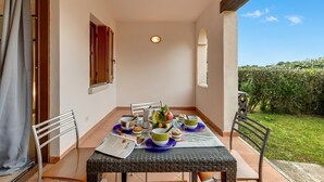 A dining table with chairs, a basket of fruit, and a candle on a balcony.