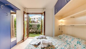 A bedroom with a bed, towels, a window, and a view of a building and greenery.