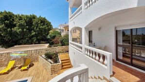 Un bâtiment blanc doté d’un balcon, un espace piscine avec des chaises jaunes et un mur en pierre.