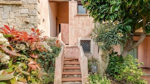 A staircase leading to a building entrance, surrounded by lush greenery and a stone wall.