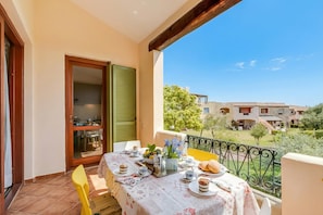 A balcony with a table set for breakfast, a sliding glass door, and a view of neighboring buildings.