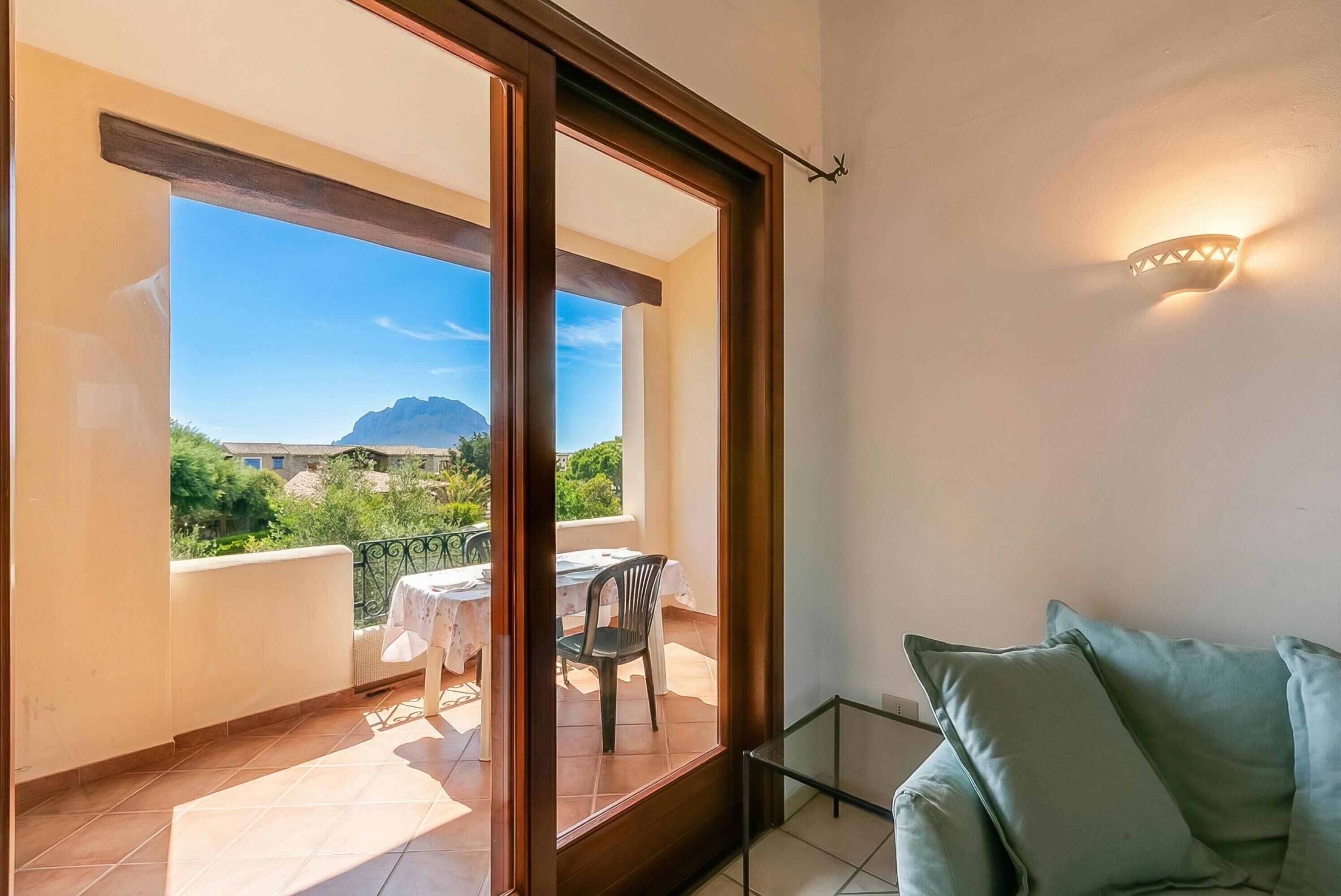 Uma varanda com mesa e cadeiras, um sofá e vista para o verde e montanhas.