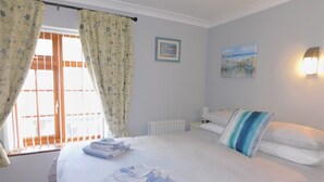 Uma cama bem arrumada com toalhas dobradas, um radiador, um quadro e uma janela com cortinas.
