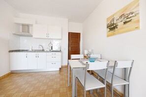 Une cuisine de taille réduite avec des meubles blancs, une porte en bois et un coin repas comprenant une table et des chaises.
