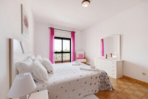 A bedroom with a bed, bedside table, dresser, and a window with curtains.