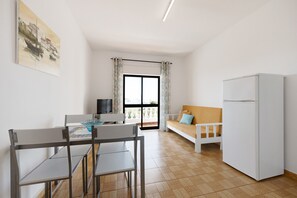 A modern kitchen with a dining table, chairs, a sofa, and a refrigerator.
