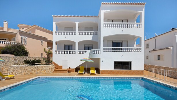 A swimming pool with a clear blue water, surrounded by a white building with balconies and yellow chairs. - Apartment 'Casa Atlântico nº2' close to the Sea with Shared Pool & Wi-Fi (Lagos)