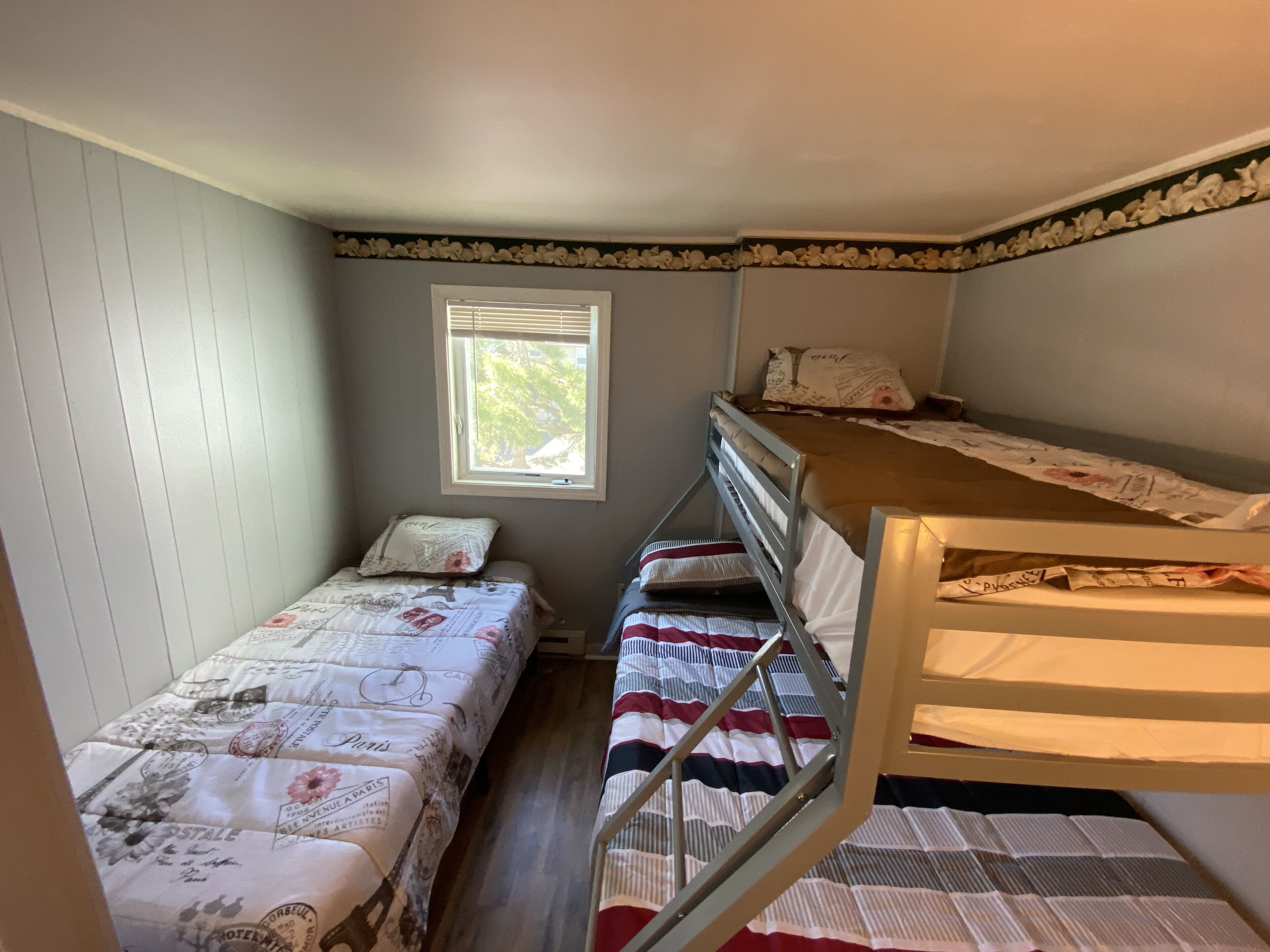A compact room with two bunk beds, a window with blinds, and a small bedside table with a lamp.