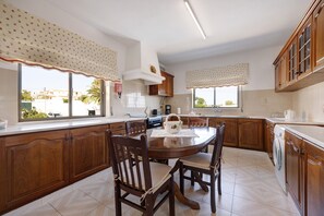 Une cuisine avec des meubles de rangement en bois, une table à manger avec des chaises, une fenêtre avec des rideaux et un lave-linge.