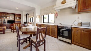 A kitchen with wooden cabinets, a dining table with chairs, a stove, and a television. - Apartment 'Casa Atlântico nº3' close to the Sea with Shared Pool & Wi-Fi (Lagos)