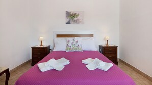Een opgemaakt bed met een roze sprei, twee nachtkastjes met lampen, een houten hoofdbord en een bloemenkussen.