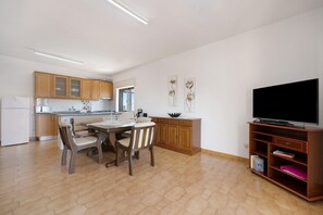 Une cuisine moderne avec des meubles en bois, une table à manger avec des chaises, un téléviseur à écran plat et une bibliothèque.